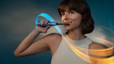 A woman smiles as she brushes her teeth using a Philips Next-Generation DiamondClean electric toothbrush.