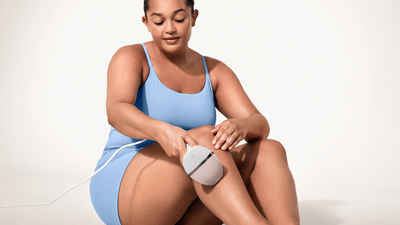 Een zittende vrouw met een blauwe bodysuit gebruikt de Philips Lumea 9900 Pro op haar benen.