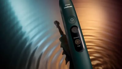 A close-up of a Philips Next-Generation DiamondClean toothbrush against a rippled blue and orange background.