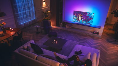 Woonkamerscène met een Philips Ambilight-tv die kleurrijk licht verspreidt terwijl een persoon ontspant op een bank