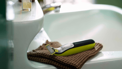 Philips OneBlade laying on top of a brown hand towel placed on the side of a bathroom sink.