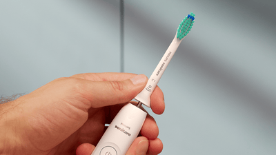 A close-up of a hand holding a white Philips toothbrush while carefully removing the Philips brush head.