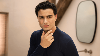 A clean shaven man wearing a navy long sleeve and posing directly at the camera with his right hand on his chin.