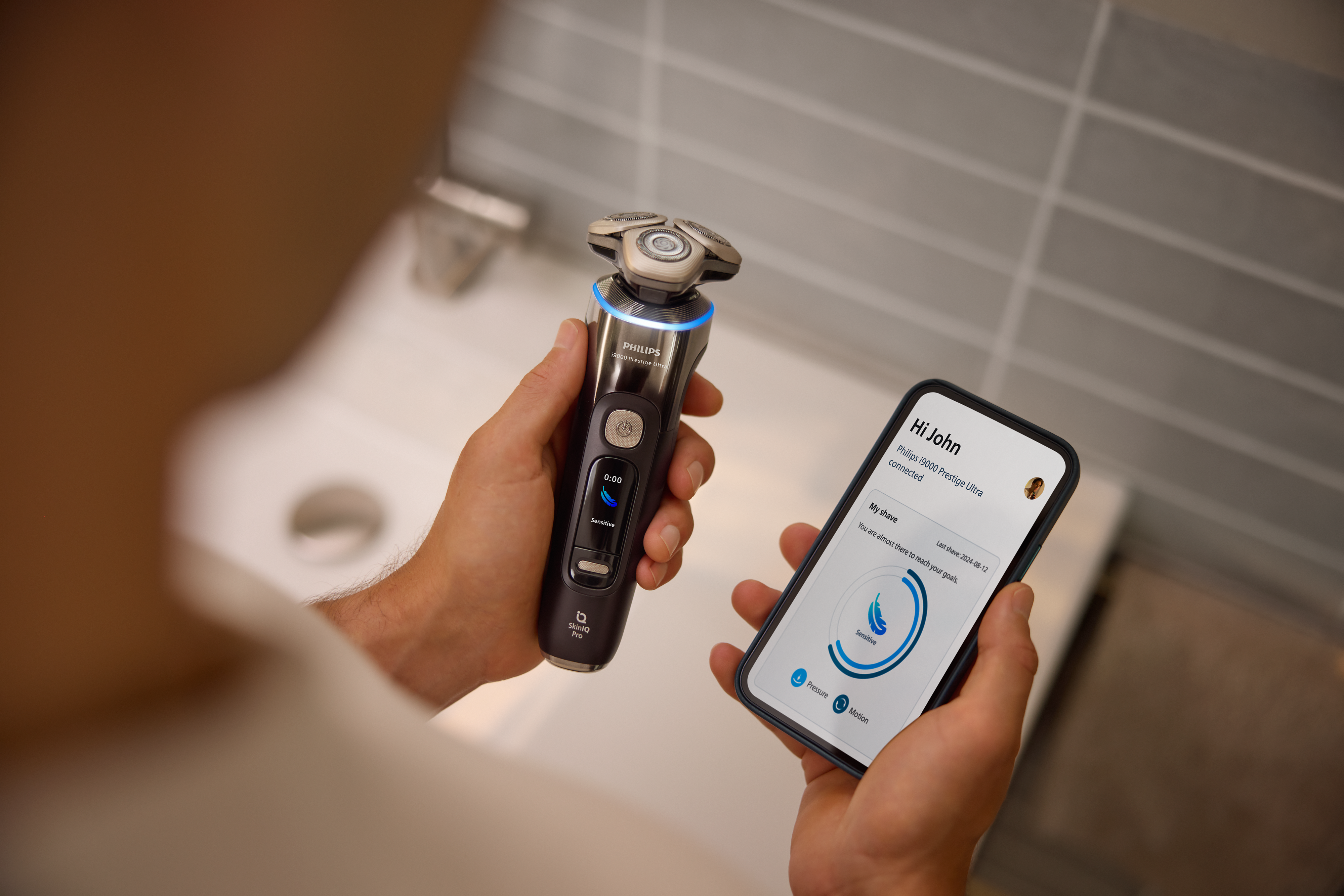 A man looking at the GroomTribe app on his phone while holding the Philips Shaver i9000 Prestige Ultra in the other hand.