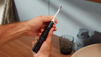 Due mani tengono uno spazzolino elettrico Philips nero con la testina bianca.