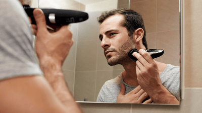 Bărbat care își tunde barba în fața oglinzii