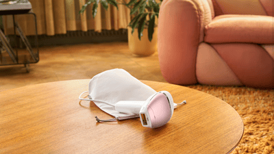 A product image of a pink Philips Lumea Sunstone 8000 on a wooden table with a cream bag.