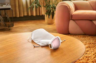 A product image of a pink Philips Lumea Sunstone 8000 on a wooden table with a cream bag.