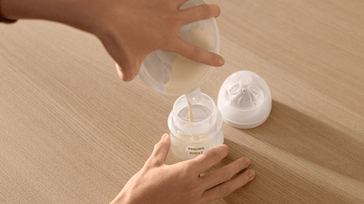 A woman empties the contents of her Philips Avent Wearable Breast Pump into an Avent Natural Response baby bottle.
