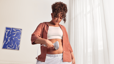 Eine Frau mit lockigen Haaren nutzt einen Philips Lumea 9900 Pro auf ihrem Bauch.