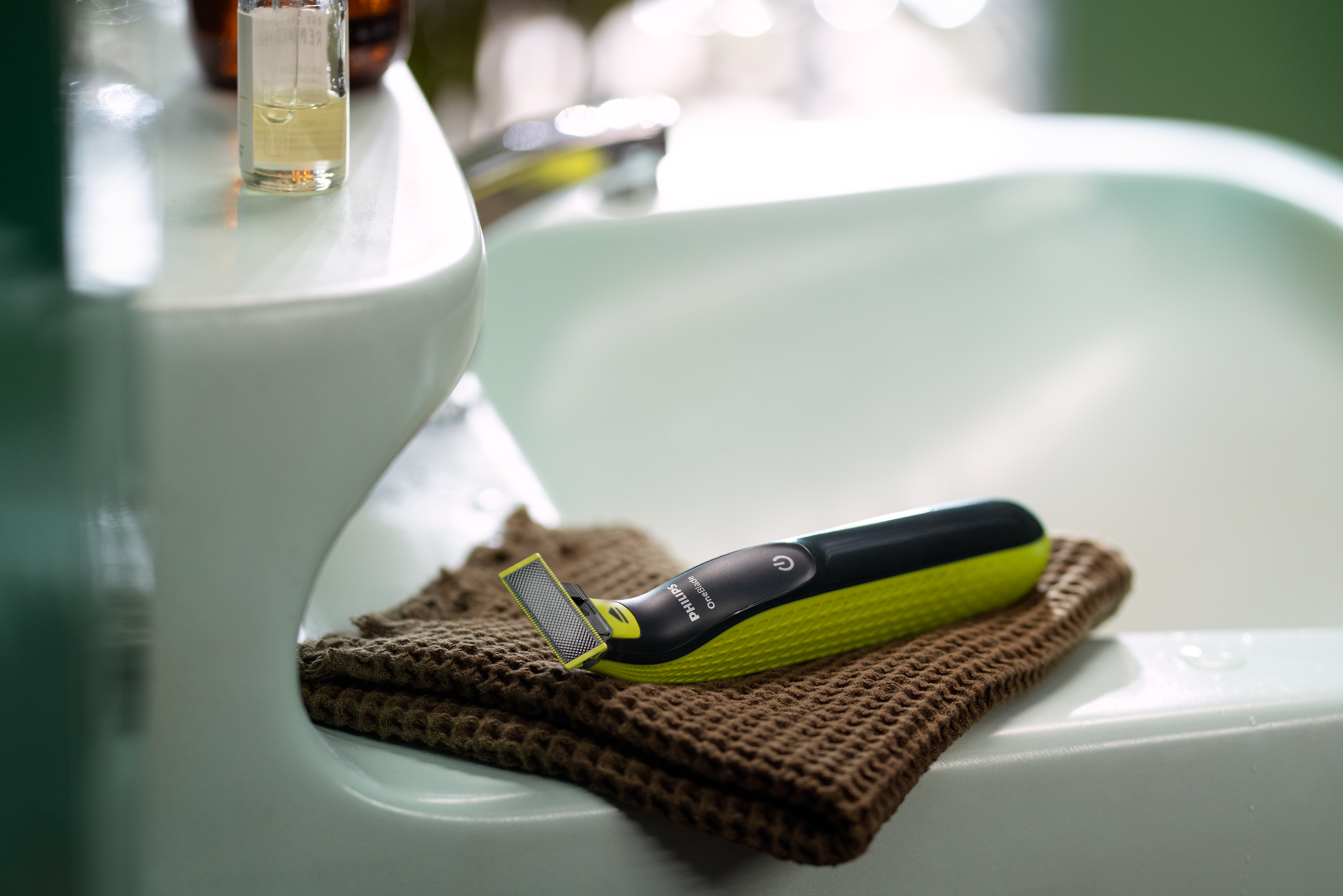 Un Philips OneBlade è appoggiato su un asciugamano marrone sul bordo del lavandino del bagno.