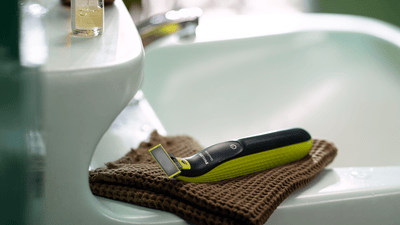 Un Philips OneBlade è appoggiato su un asciugamano marrone sul bordo del lavandino del bagno.