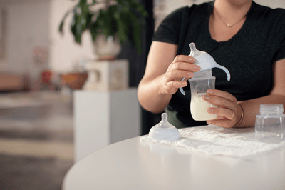 Een moeder in een zwart T-shirt doet een speen op een Philips Avent-babyfles waar afgekolfde melk in zit.
