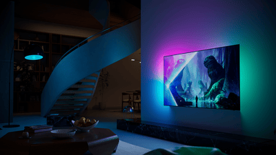 Philips Ambilight TV mounted on a wall in a modern living room, casting colorful ambient light that matches the vivid fantasy scene displayed on screen.