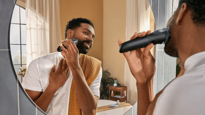 A man is shaping and trimming his beard in front of his bathroom mirror using a Philips beard trimmer.