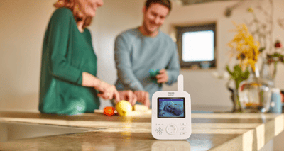 A Philips Video monitor sitting on a kitchen counter, pictured in front of a blurred background of a couple cooking.