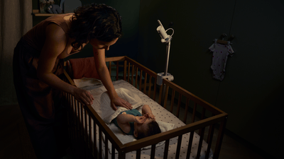 Una mujer mirando a su bebé en la cuna en una habitación con poca luz, junto al vigilabebés Philips Avent Premium.