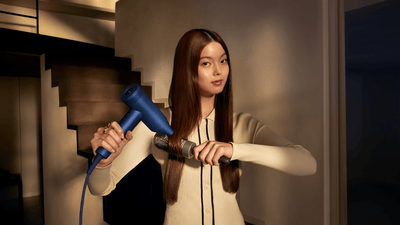 Une femme utilise le sèche-cheveux Philips série 8000 bleu et une brosse ronde pour sécher ses cheveux lisses.
