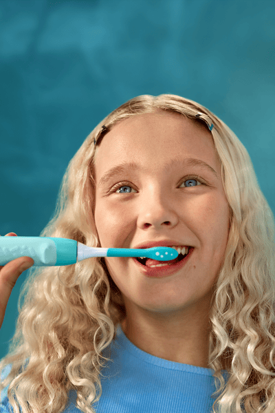 A blonde girl brushing her teeth with an electric toothbrush