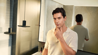 A cleanly shaven man poses directly at the camera with his left hand on his chin.