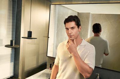 A cleanly shaven man poses directly at the camera with his left hand on his chin.