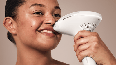 Une jeune femme sourit en utilisant le Philips Lumea 9900 Pro qui élimine les poils de sa lèvre supérieure.