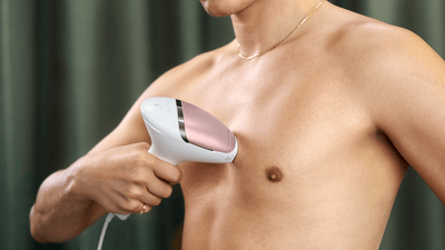 A man uses a Philips Lumea IPL device to remove hair on his bare chest.