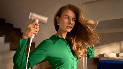 Žena si suší vlasy ve sluncem zalité koupelně