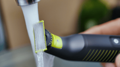 Product close-up image of a Philips OneBlade under running water to clean the razor.
