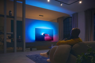 Person schaut einen Philips Ambilight Fernseher, blaues und rotes Ambient-Licht an der Wand.