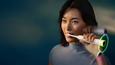 A young woman brushes her teeth using a Philips Next-Generation DiamondClean electric toothbrush.