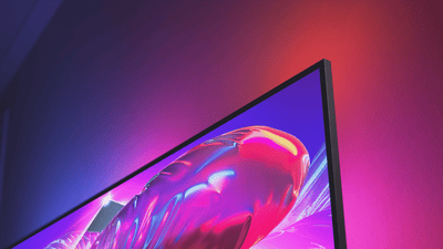 Close-up of a Philips Ambilight TV with an ultra-thin bezel, displaying vibrant pink and purple visuals while matching ambient light glows on the wall behind it.