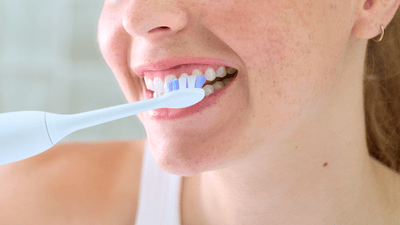 A close-up of a young woman in a white top brushing her teeth with a white Philips electric toothbrush.