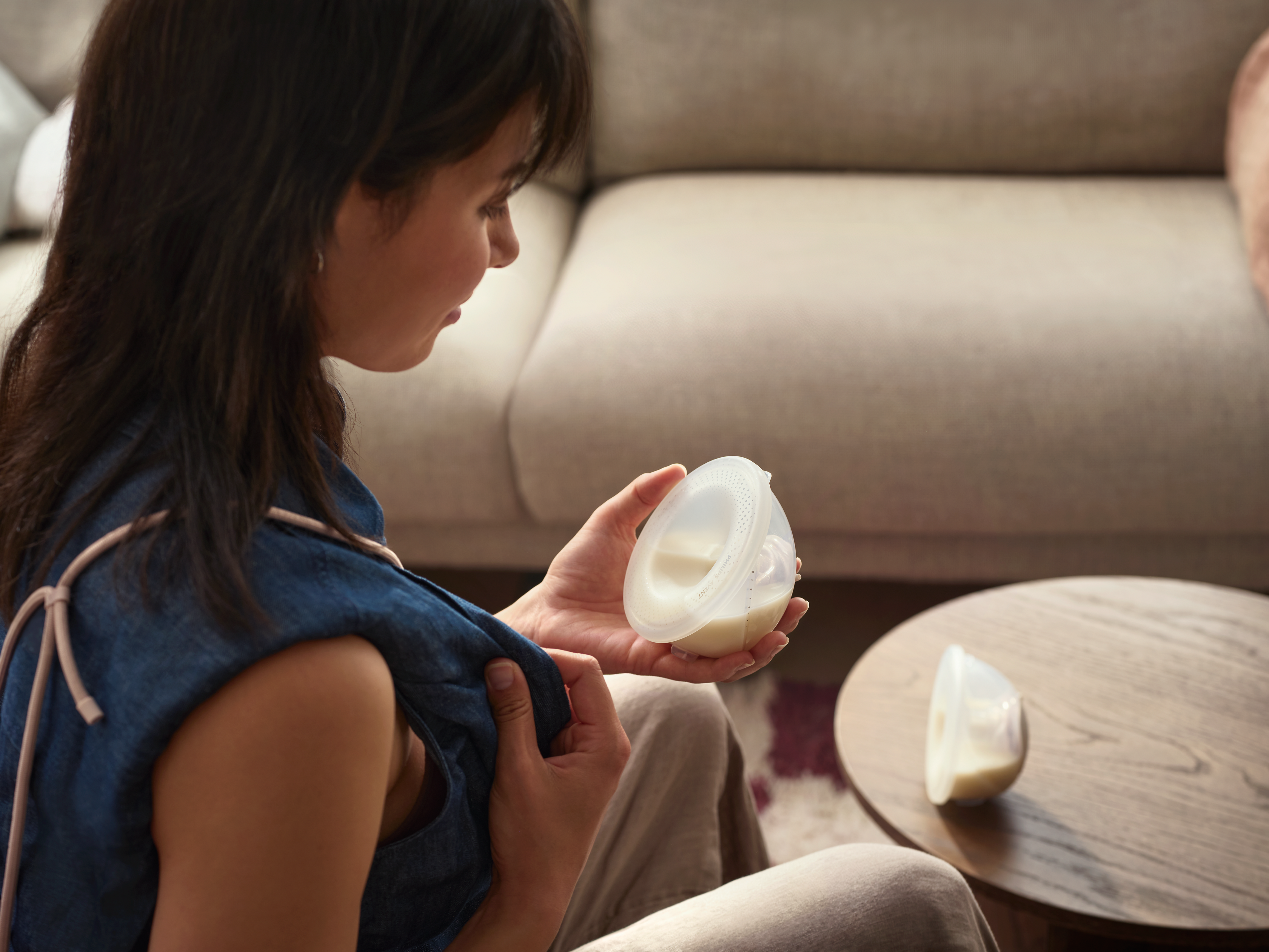 A woman attaching her hands-free breast pump at home, whilst sitting on a chair.