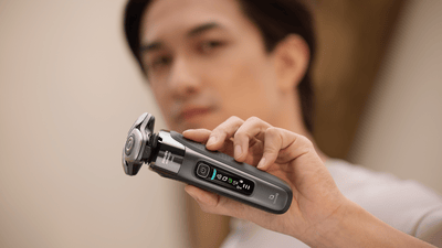Product close-up of a man holding up a grey Philips shaver towards the camera.