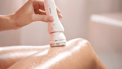 A close-up of a woman exfoliating her legs with a white Philips device.
