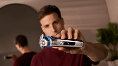 Product close-up image of a man holding up a blue Philips shaver towards the camera.