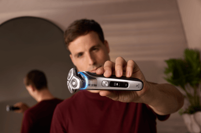 Product close-up image of a man holding up a blue Philips shaver towards the camera.