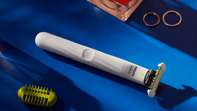 The Philips OneBlade Intimate lying on a dark blue surface next to it’s trimming attachment.