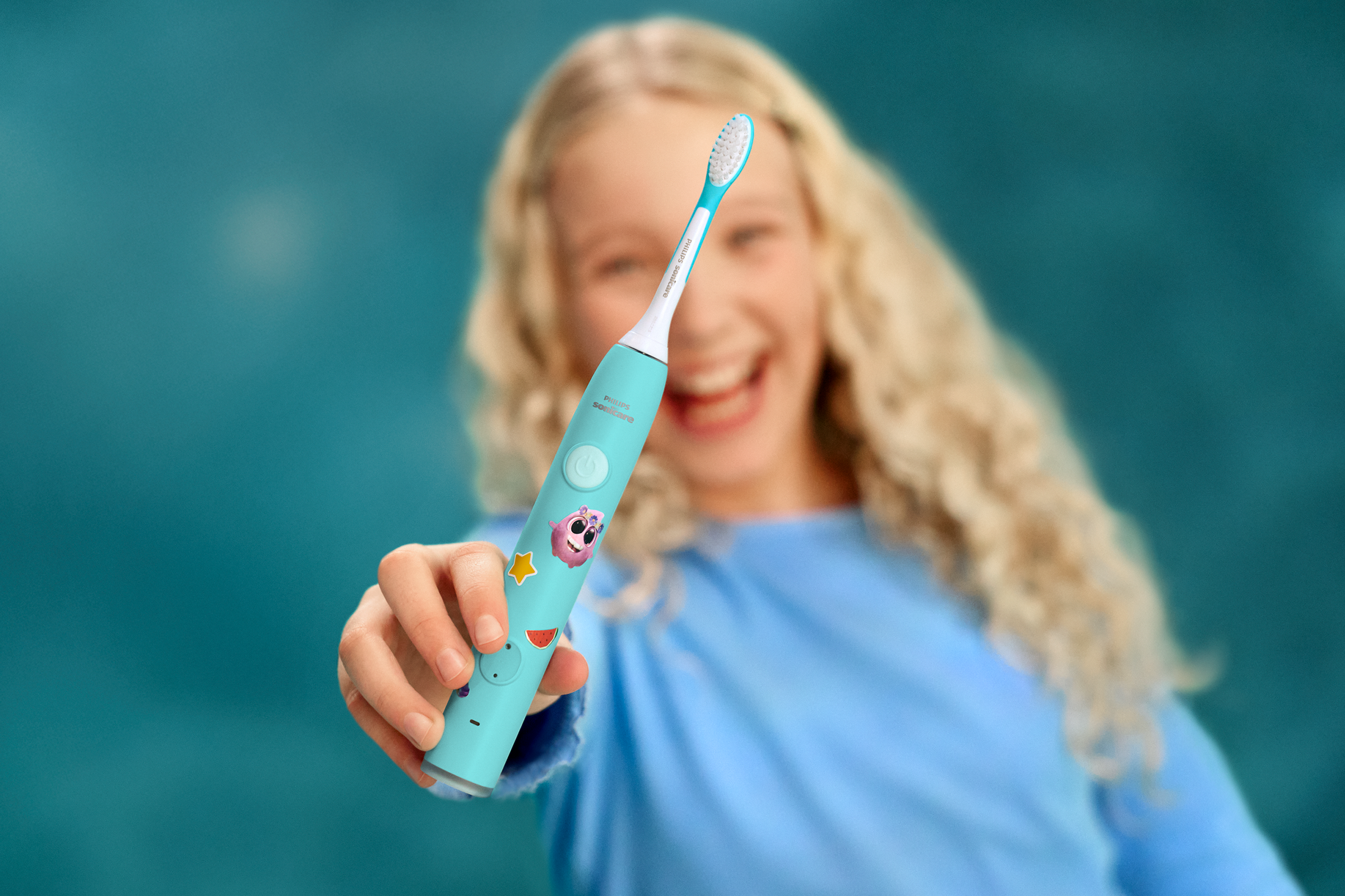 Child showing off smile while holding a Sonicare For Kids power toothbrush.