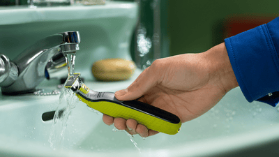 Water running out of a tap to clean a Philips OneBlade in a white sink.