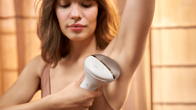 A young woman with shoulder long brown hair is using her Philips IPL Lumea on her underarms.