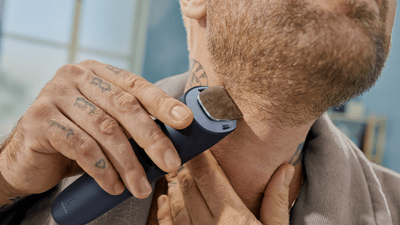 A close up picture of a man`s face capturing him shaving his beard using a Philips OneBlade.