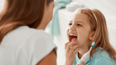 Child brushing teeth with parent's guidance