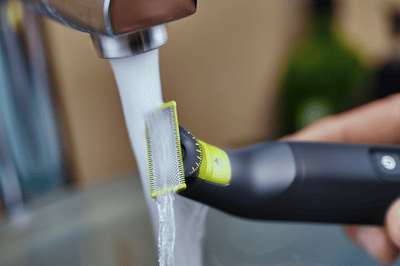 Een close-upfoto van een Philips OneBlade die onder de kraan wordt afgespoeld.