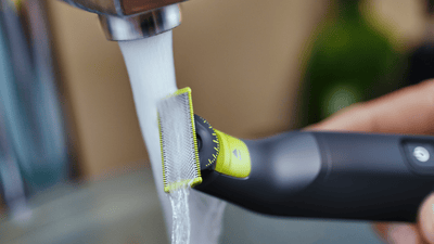 A close up picture of a Philips OneBlade being washed under a faucet.