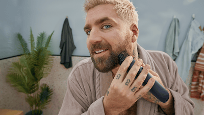Un uomo con i capelli biondi e la barba scura si sta tagliando la barba completa con un regolabarba Philips.