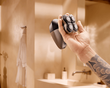 Philips head shaver held in tattooed hand in bathroom