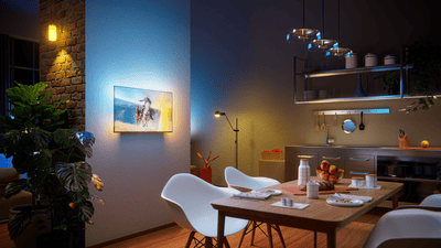 Philips Ambilight TV mounted in a modern open-plan dining and kitchen space, displaying a horseback riding scene with warm and cool ambient lighting extending onto the wall behind the screen.