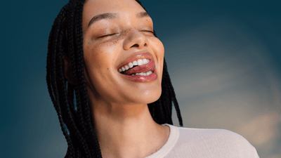 A young woman with sparkly white and clean teeth is licking her tongue over her teeth.